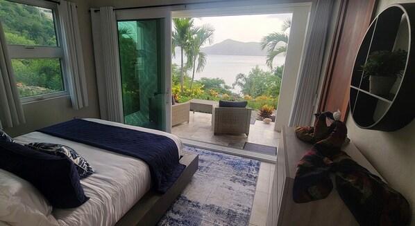 Een slaapkamer met een groot bed, een schuifdeur naar een balkon met uitzicht op zee en bergen.