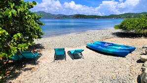 A beach with kayaks, chairs, and a rocky shoreline. - BEACHFRONT 5 BEDROOM VILLA–POOL, SOLAR, PRIVATE (East End)