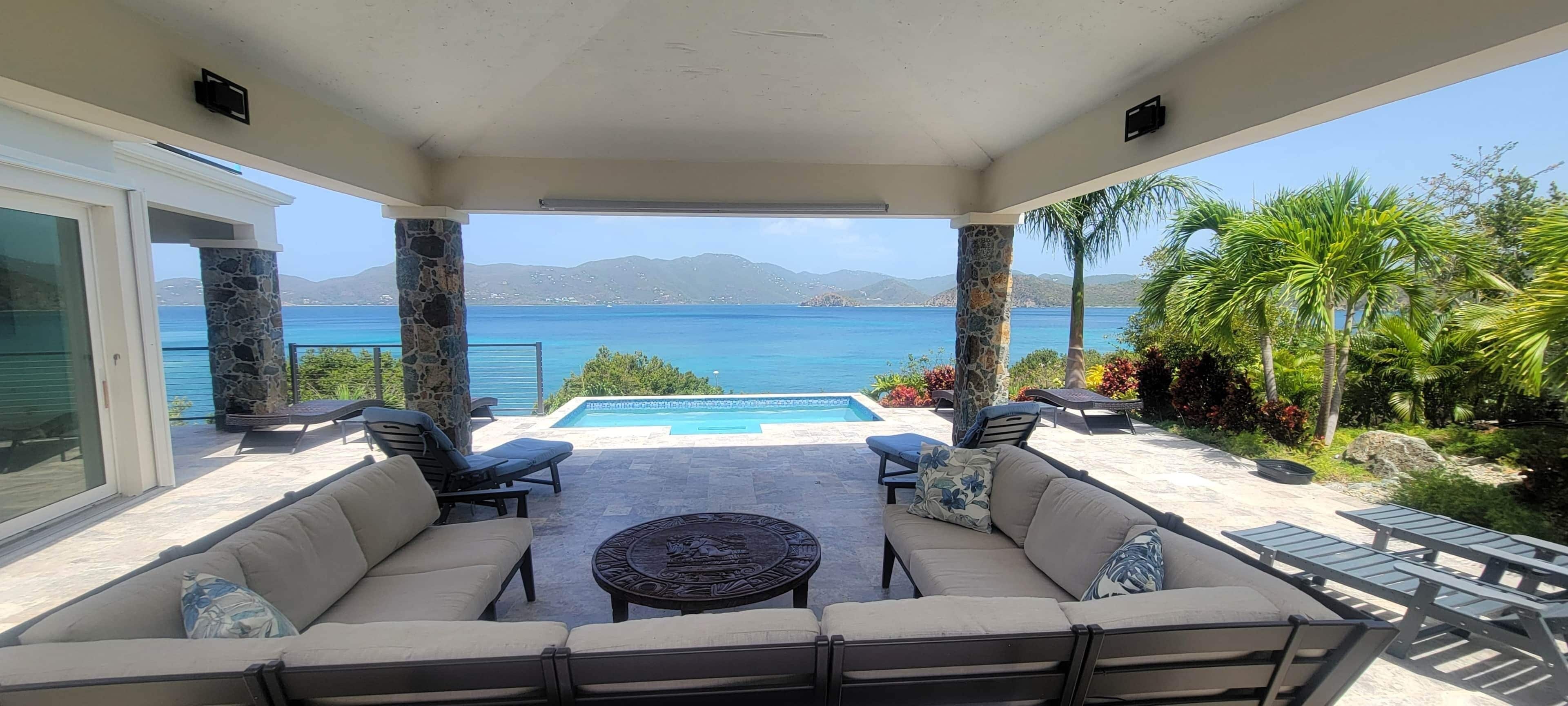 Ein überdachter Außenbereich mit Pool, Liegestühlen und Blick aufs Meer.