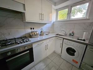 A kitchen with a gas stove, oven, washing machine, and a window above the sink. - Islington Flat close to King’s Cross (Greater London)