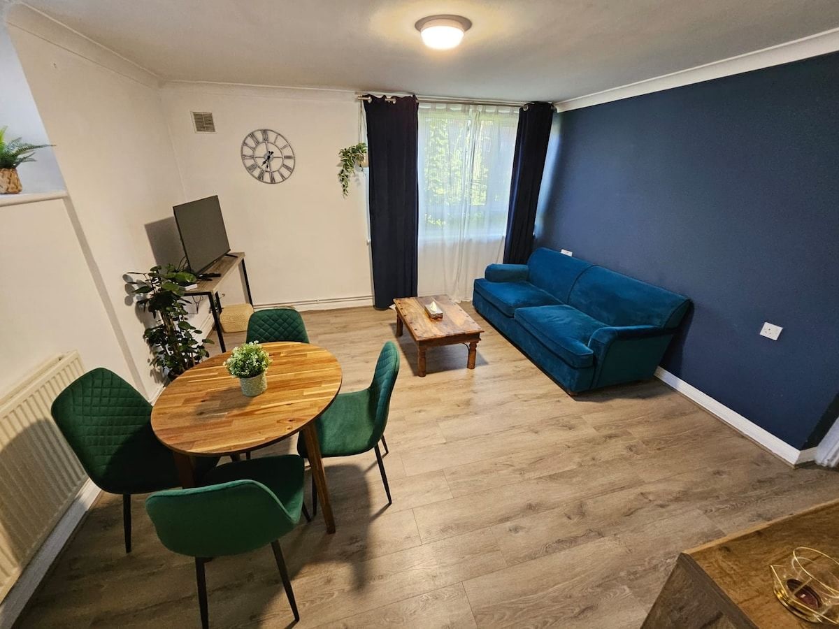 A living room with a blue sofa, a wooden coffee table, a dining table with chairs, and a clock on the wall.