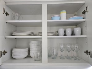 A white cabinet with shelves containing plates, bowls, cups, and glasses. - Islington Flat close to King’s Cross (Greater London)
