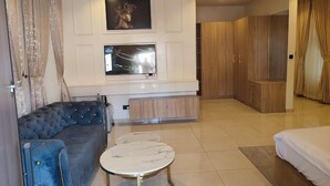 A modern living room with a blue sofa, a round coffee table, a TV mounted on the wall, and wooden cabinets. - El-Castillo Hotels and Suites Lekki (Lekki)