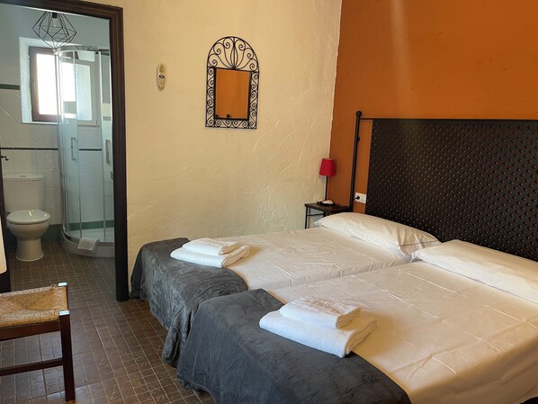Quarto de hotel com duas camas, chuveiro, vaso sanitário e um espelho na parede.