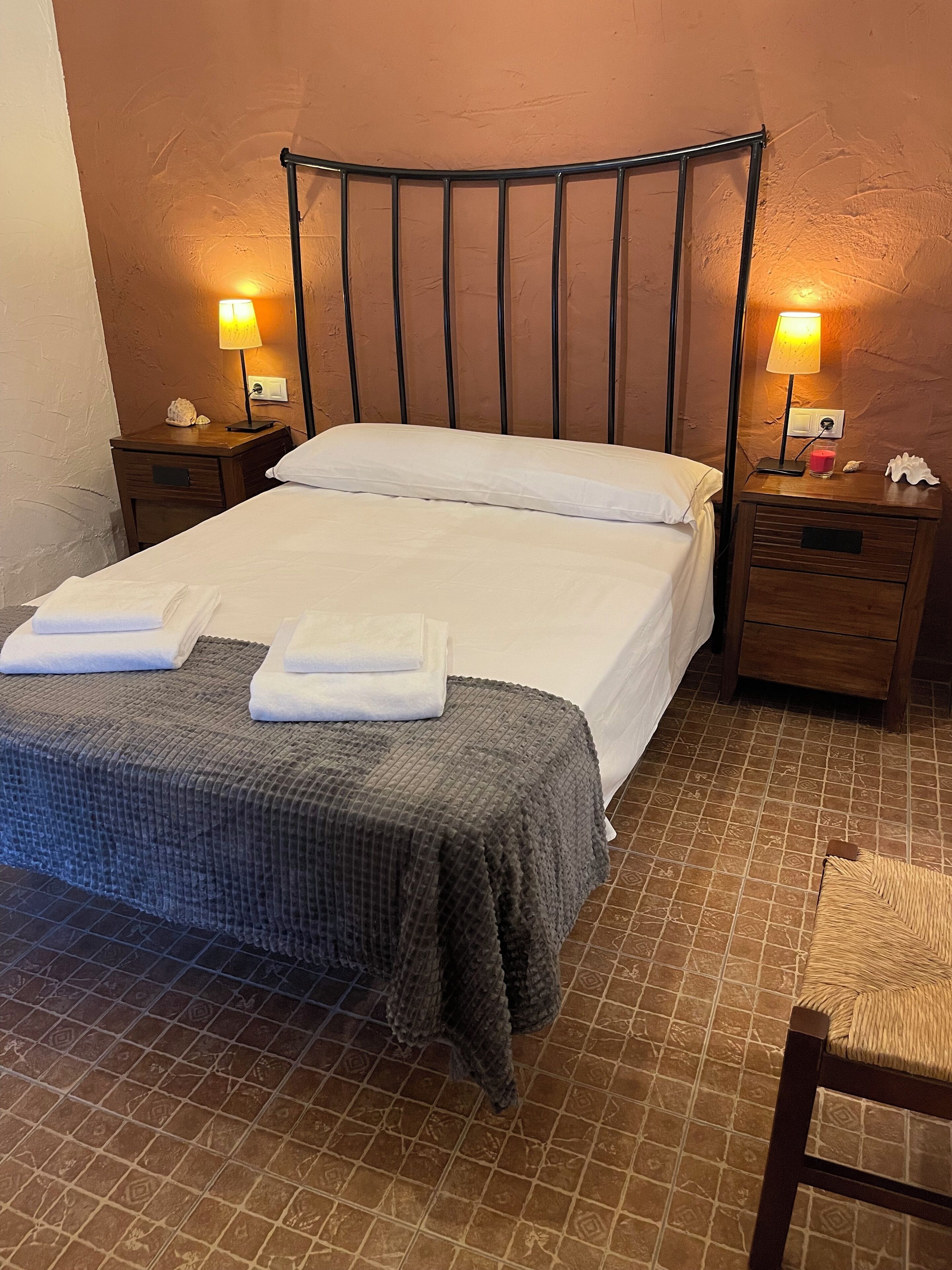 A neatly made bed with a metal headboard, two bedside tables with lamps, and a tiled floor.