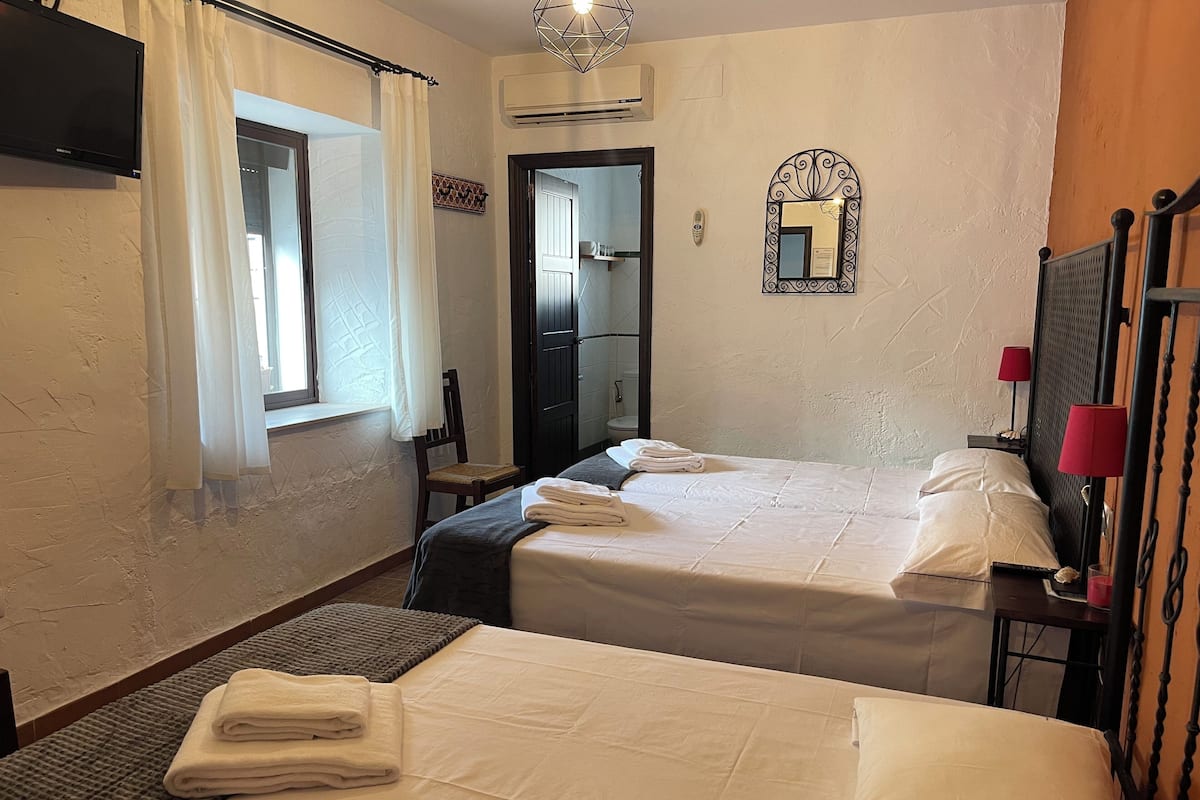 Habitación de hotel con dos camas, una ventana con cortinas, un espejo y una lámpara roja en la mesita de noche.