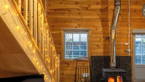 A cozy cabin interior with a wood-burning stove, a TV, and string lights. - Walliswood Lodge - Rural Retreat - Newly converted, Wood Burner, Air Con, wi-fi (Dorking)
