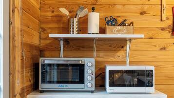A kitchen with wooden walls, a white radiator, and two microwaves on a shelf.