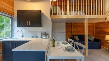 A modern kitchen with a central island, a dining area with a table set for two, and a loft bedroom with a wooden railing.