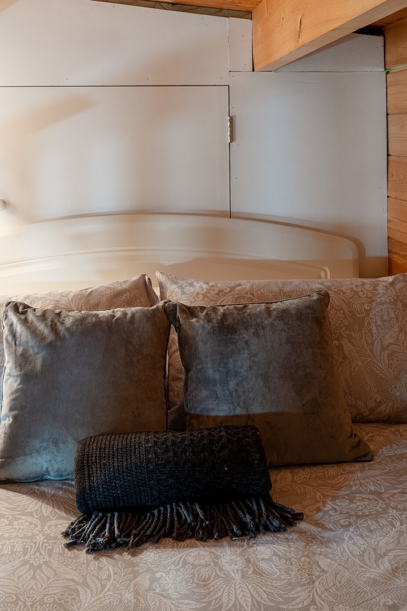 Rincón de una habitación con una cama, dos almohadas y un plaid de punto.