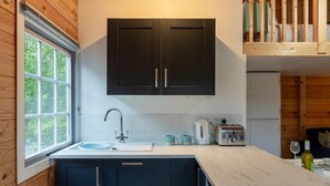 A modern kitchen with dark cabinets, a white countertop, a sink, and a window. - Walliswood Lodge - Rural Retreat - Newly converted, Wood Burner, Air Con, wi-fi (Dorking)