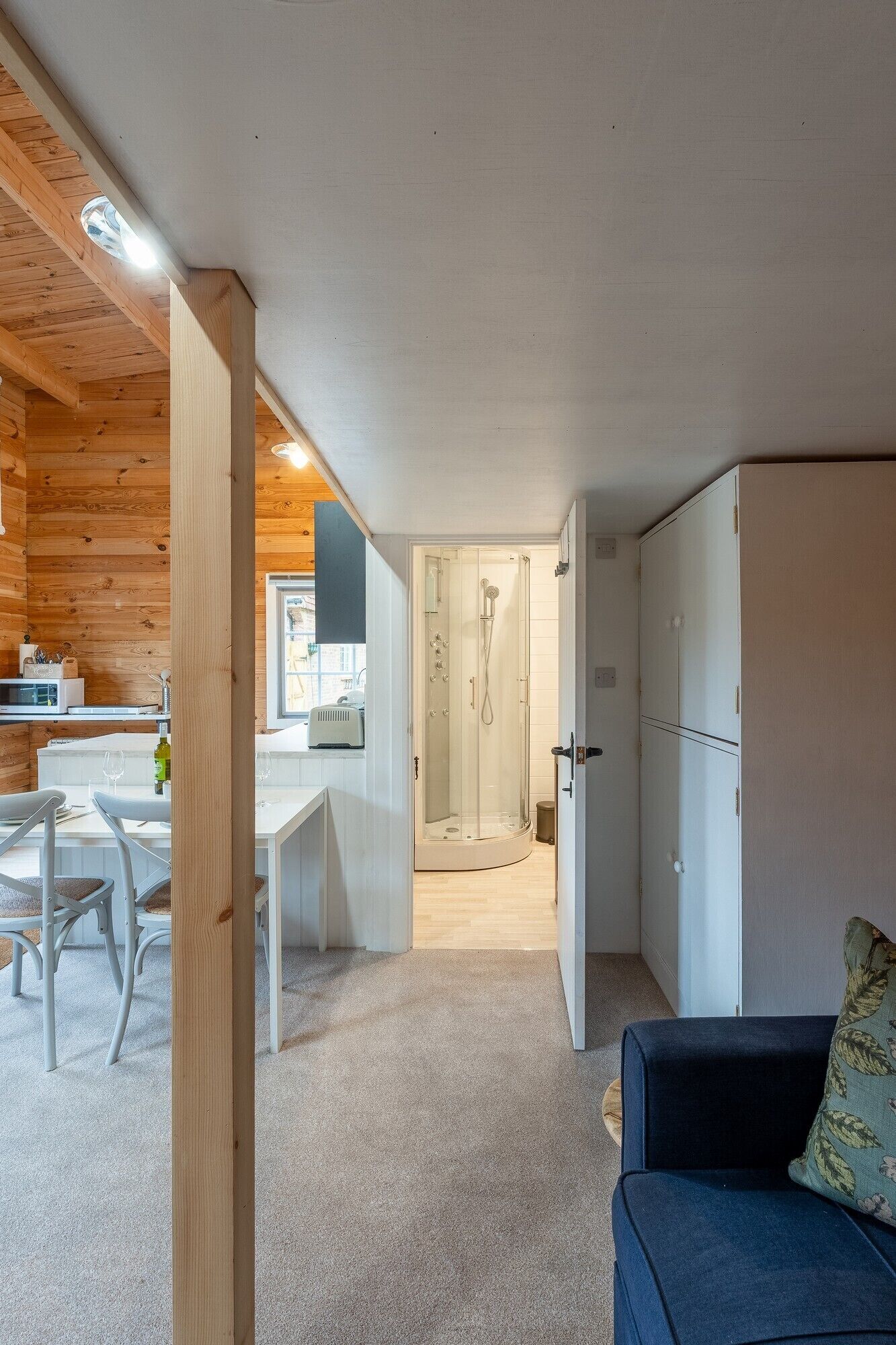 Et kompakt, moderne værelse med trælofter, et tekøkken, bruser og opholdsområde med sofa og bord.