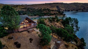 Una baita con una veranda che si affaccia su un lago, circondata da colline e alberi.