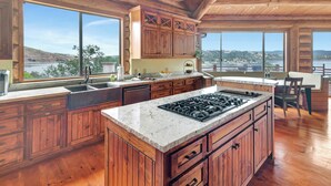 Un'ampia cucina con mobili in legno, una grande isola con piano cottura e ampie finestre che offrono vista sul paesaggio.
