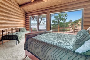 A log cabin bedroom with two beds, a large sliding glass door leading to an outdoor deck, and a view of a mountainous landscape.