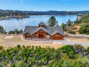 A log cabin with a garage, a driveway, and a view of a lake and hills.