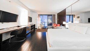 A modern hotel room with a large bed, a desk with a chair, a television, and a view of the city through large windows. - 50th Floor High rise with 180° Strip Views + Open Balcony - No Resort Fees (Las Vegas)