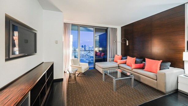 A modern hotel room with a sofa, armchair, and a flat-screen TV mounted on the wall. - 50th Floor High rise with 180° Strip Views + Open Balcony - No Resort Fees (Las Vegas)