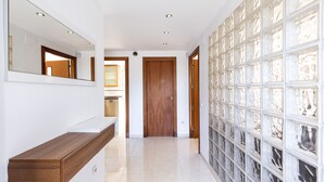 Un pasillo con una puerta de madera, una pared blanca con un espejo y una pared de bloques de vidrio con un diseño decorativo.