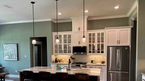 A modern kitchen with a large island, bar stools, white cabinets, stainless steel appliances, and pendant lighting. - Beautiful New 4-bedroom home on Granada Golf Course in Hot Springs Village. (Hot Springs Village)