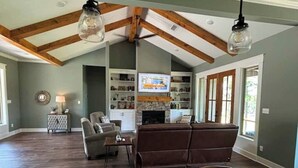 A spacious living room with a high ceiling, built-in shelving, a fireplace, and a large window. - Beautiful New 4-bedroom home on Granada Golf Course in Hot Springs Village. (Hot Springs Village)