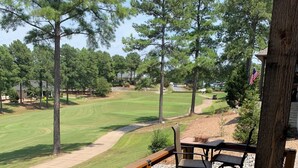 A wooden deck with a stone pillar, overlooking a golf course with trees and a clear sky. - Beautiful New 4-bedroom home on Granada Golf Course in Hot Springs Village. (Hot Springs Village)