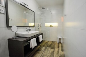 Casa de banho moderna com um espelho grande, uma pia, um chuveiro e um banquinho pequeno.