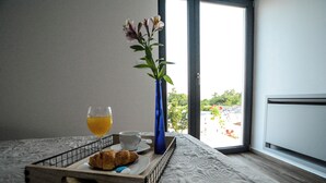 Ein Frühstücksbrett mit Croissants, einem Glas Orangensaft und einer Tasse auf einem Bett mit Blick auf Grünflächen.