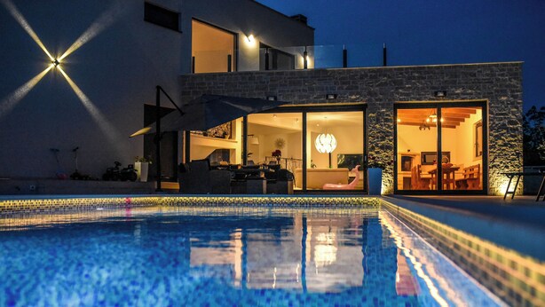 Ein modernes Haus mit Swimmingpool, großen Fenstern und einem gut beleuchteten Innenraum.
