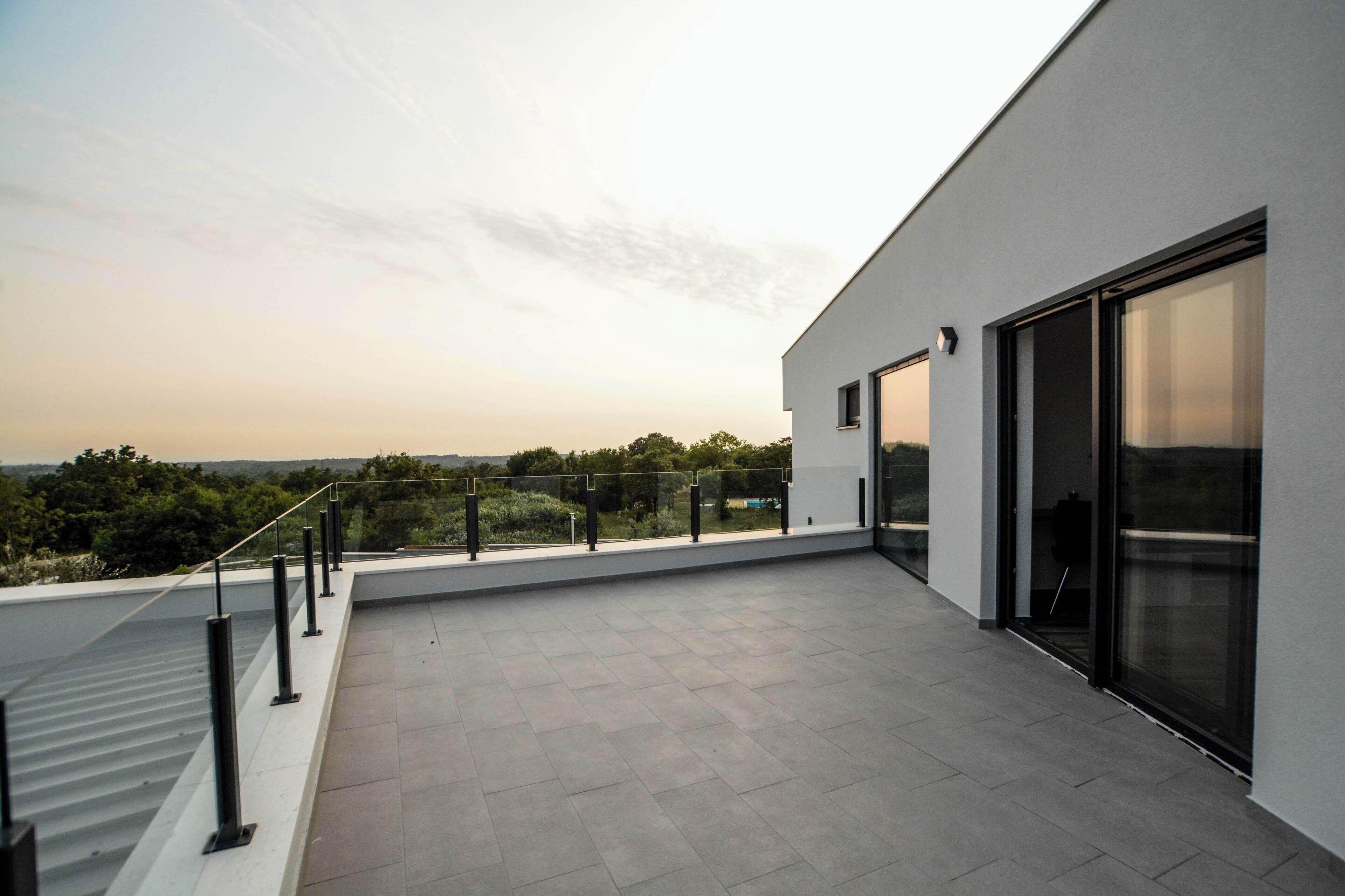 A modern building with a flat roof terrace, large sliding glass doors, and a view of the surrounding landscape.