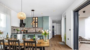 A modern kitchen with teal cabinets, a wooden dining table set for six, and a large window providing natural light. - Villa Endi 4* with swimming pool in Medulin (Medulin)