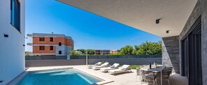 Une piscine sur le toit, avec des chaises longues et une table, entourée d’une haute clôture et bordée de bâtiments en arrière-plan.