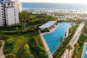 Un resort con una piscina grande, palmeras y vistas al océano.