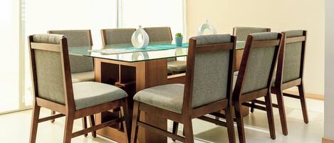 A dining area with a glass-top table surrounded by six wooden chairs with cushioned seats.