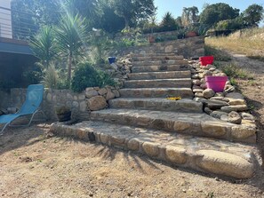 Steps lead to a serene garden area surrounded by potted plants and a stone wall.