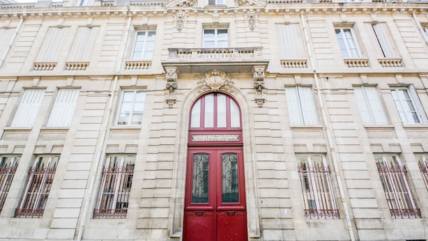 Ein historisches Gebäude mit einer markanten roter Tür, symmetrischen Fenstern und klassischen architektonischen Details.
