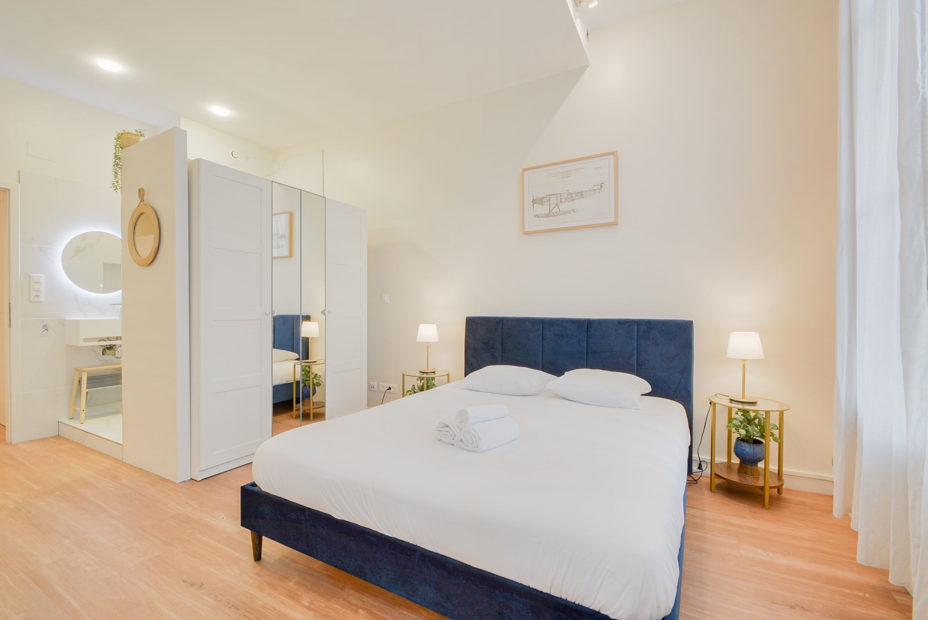 A modern bedroom with a large bed, a wardrobe, a mirror, and a framed picture on the wall.
