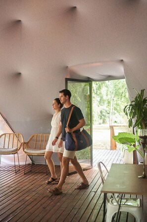 A couple walking on a wooden deck with wicker chairs and a table, under a large tent-like structure. - Brisas del lago Glamping (Partido de Tigre)