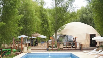 A pool area with lounge chairs, a tent, and a dining setup.