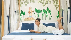 A bed with a canopy, a wall mural, and two wicker chairs.