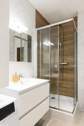 Ein modernes Badezimmer mit einer gläsernen Duschkabine, einem weißen Waschtisch und einer Wand in Holzoptik.