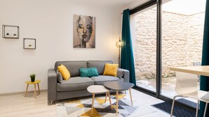 En moderne stue med en grå sofa, gule og turkise puder, et lille sofabord med en plante og en måtte med geometriske mønstre.