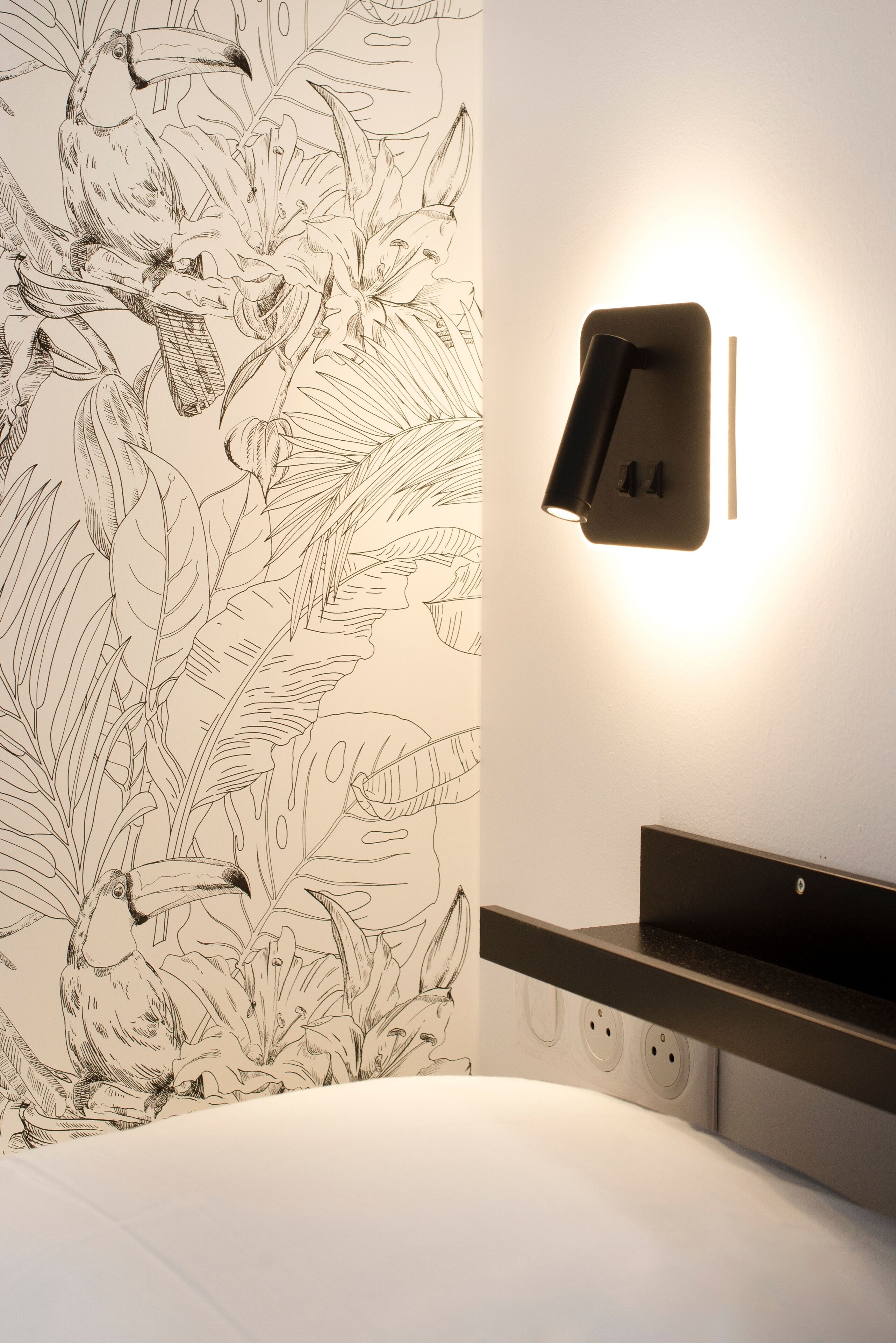A bedroom with a wall-mounted light fixture, a bed, and a power outlet.