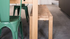 Ein moderner Essbereich mit einem Holztisch, grünen Stühlen, einer Vase mit Zitronen und einer Steinsäule.