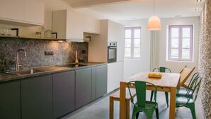 Eine moderne Küche mit Marmorarbeitsplatte, Edelstahlgeräten und einem Essbereich mit Holztisch und grünen Stühlen.