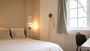 Ein Schlafzimmer mit Bett, Schreibtisch, Stuhl, Heizkörper und einem fenster mit Vorhängen.