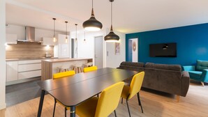 A modern kitchen with a dining area, a sofa, and a TV mounted on the wall. - Le Spacieux de Dizier - Proche place des Vosges (Nancy)