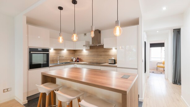 A modern kitchen with a central island, bar stools, pendant lighting, and a view to the living area. - Le Spacieux de Dizier - Proche place des Vosges (Nancy)