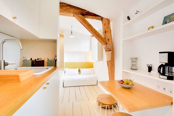Una cocina moderna con detalles de madera, un comedor con un frutero y una cama al fondo.