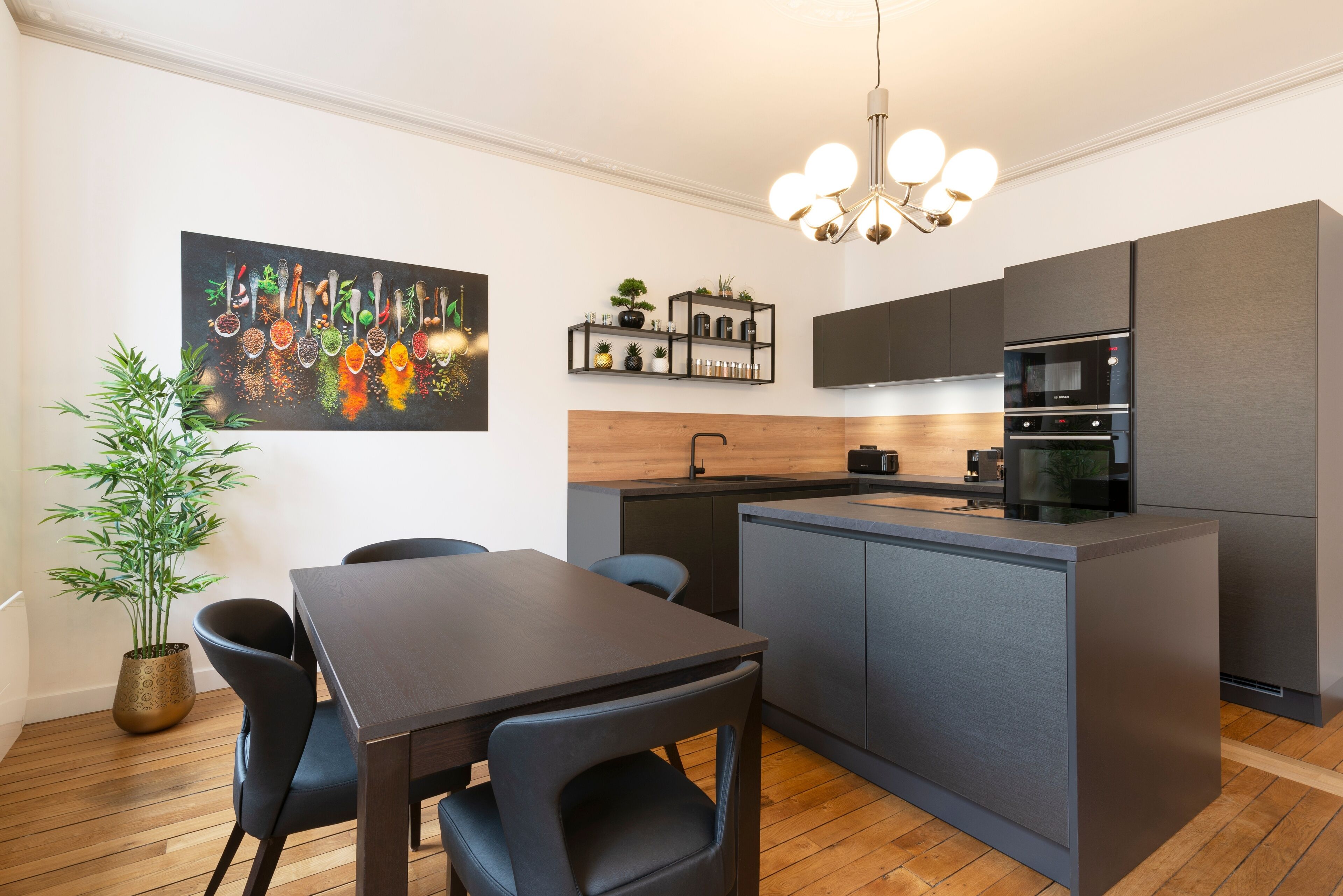 Une cuisine moderne avec un îlot central en bois, des meubles de rangement aux couleurs sombres et un luminaire suspendu.